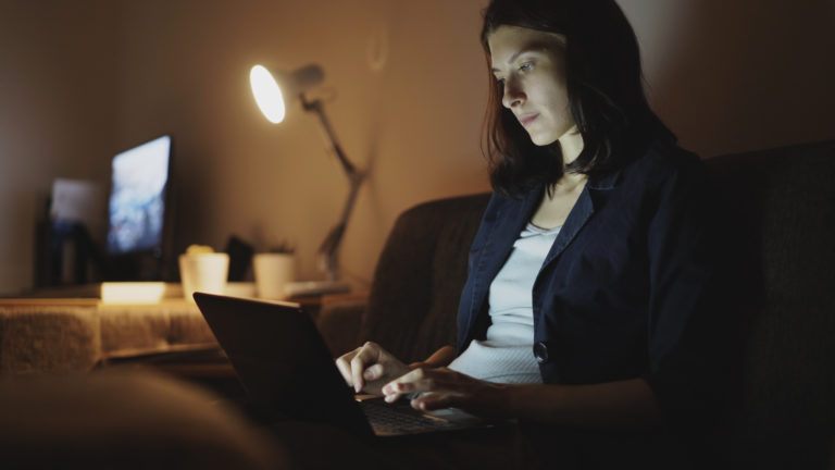 Young concentrated woman working at night using laptop computer and typing message